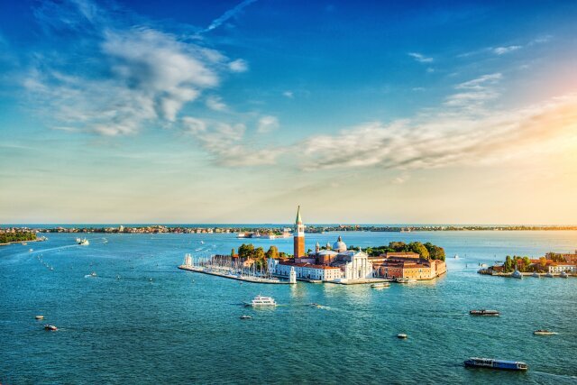 Aerial view of the lagoon of Venice and San Giorgio Maggiore at Sunset. Heavy ship traffic, turistic boats and beautiful blue sky with fantastic cloudscape over the island. Venice, Italy.