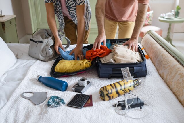 A couple packing a suitcase with clothing, reusable water wattles and other travel items