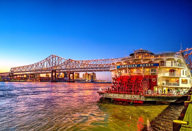 American Queen Voyages cruise ship on the Mississippi River in New Orleans at dusk.