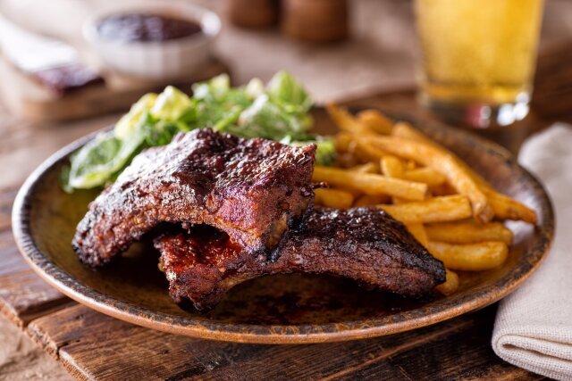 A plate of delicious barbecued ribs with french fries and salad.