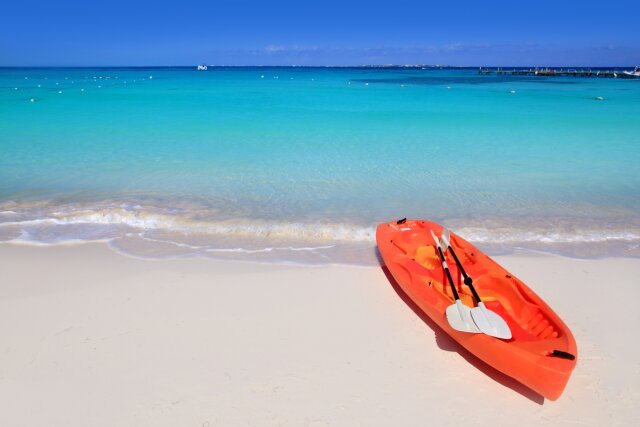 Orange kayak with paddles inside on a Caribbean beach with turquoise water.